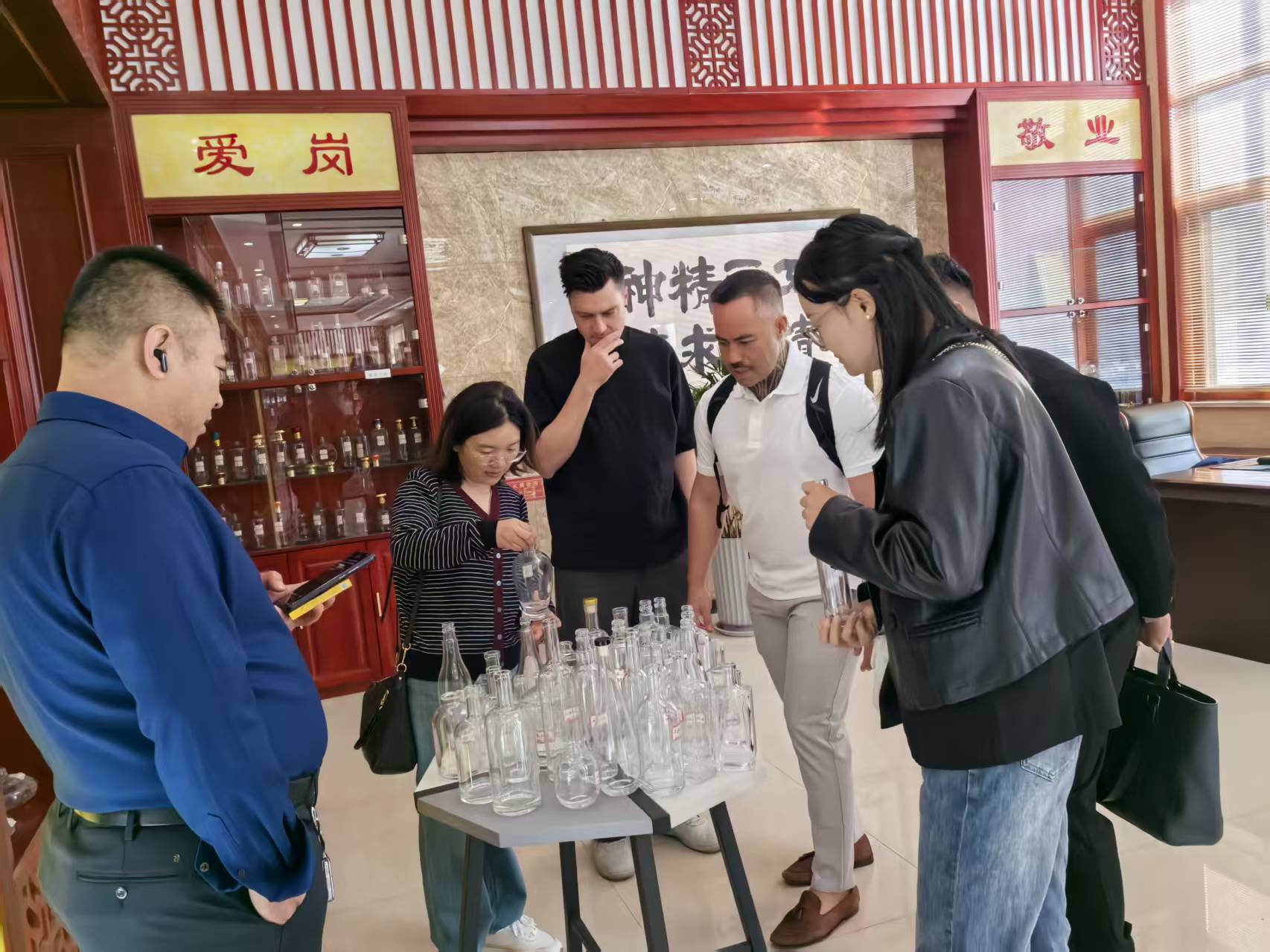 Visitors examine clear bottles and containers arranged on a display table in a Chinese-themed showroom.