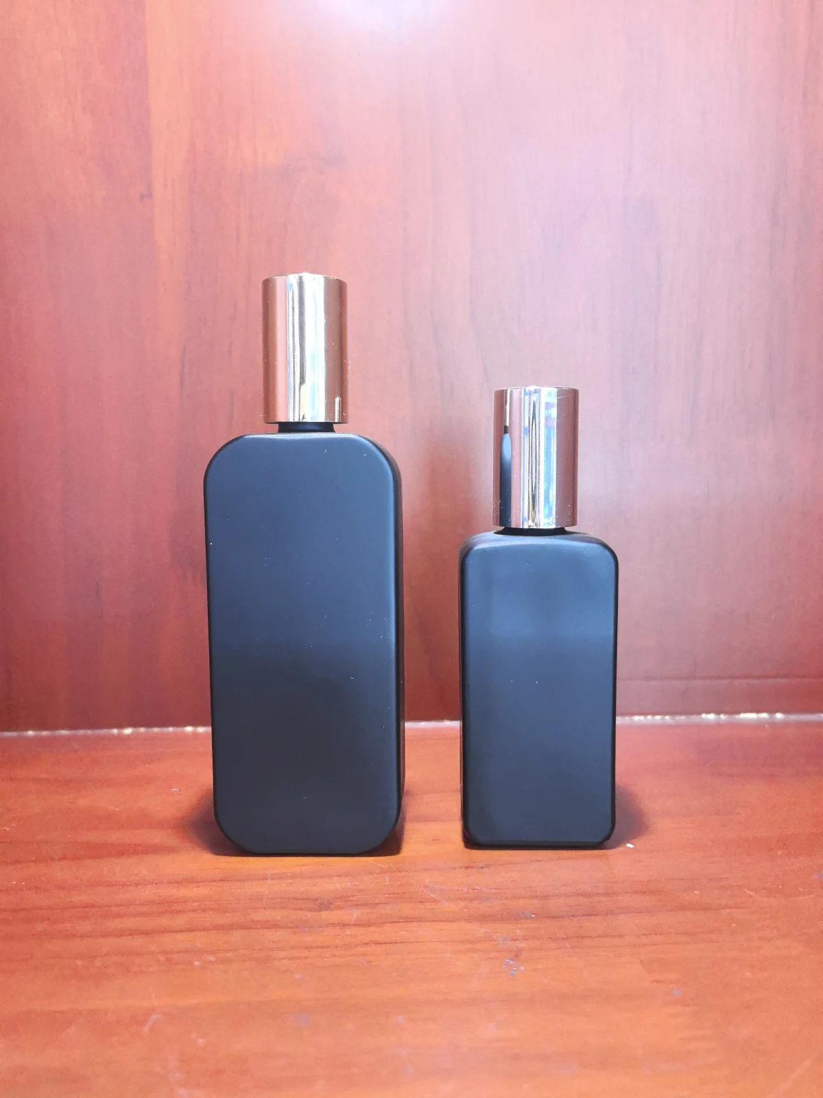 Two dark rectangular bottles with reflective cylindrical caps on a wooden surface.