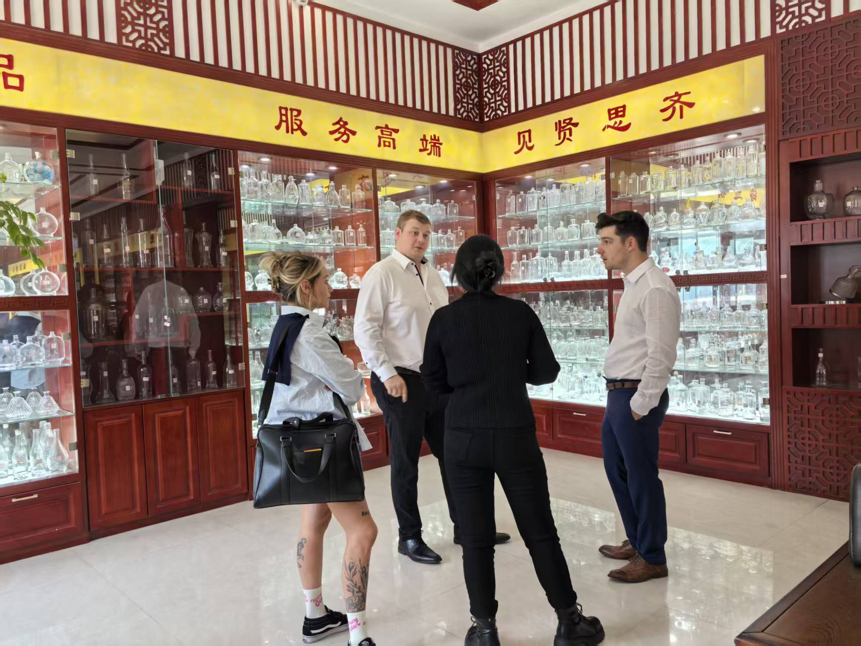Glass bottles and containers arranged in illuminated wooden showroom cabinets with four people standing in front.