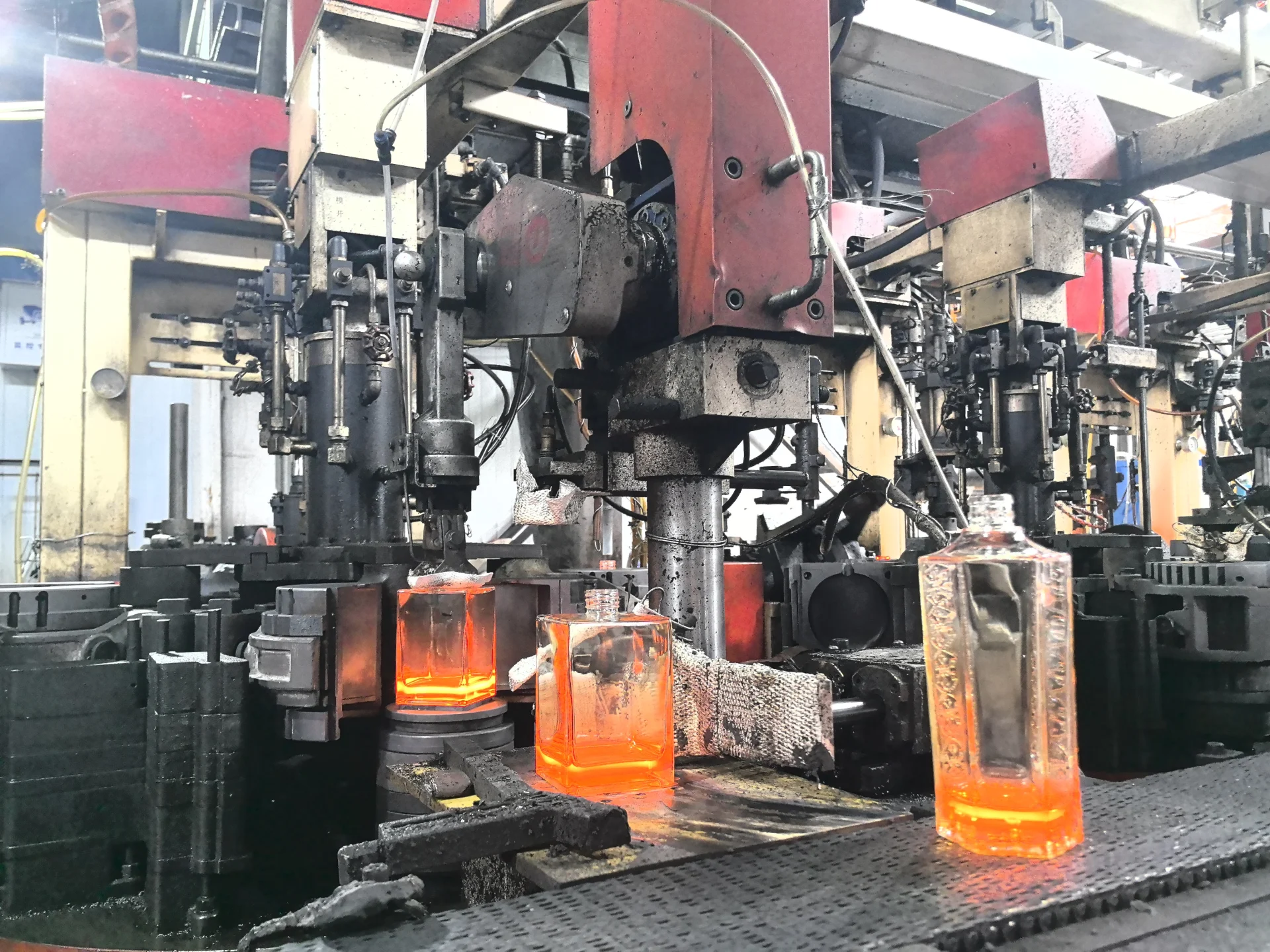 Hot square glass containers moving through industrial forming machinery on a production line
