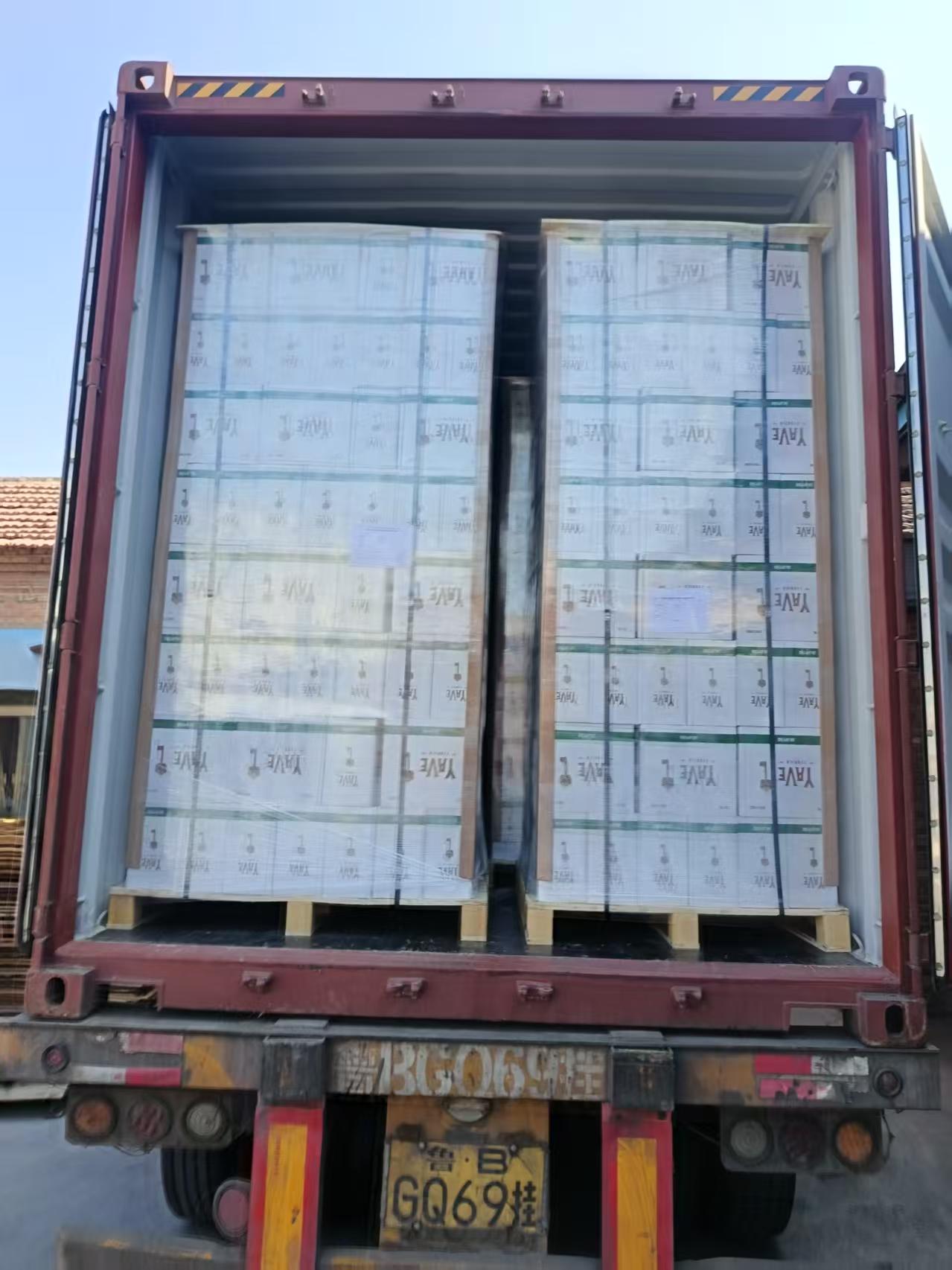 Two plastic-wrapped palletized stacks of printed cartons inside an open shipping container on a truck.