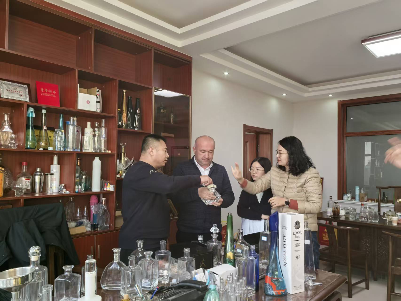 People gather around a table displaying Royal Elite Supreme Vodka packaging and assorted bottles in an indoor showroom.